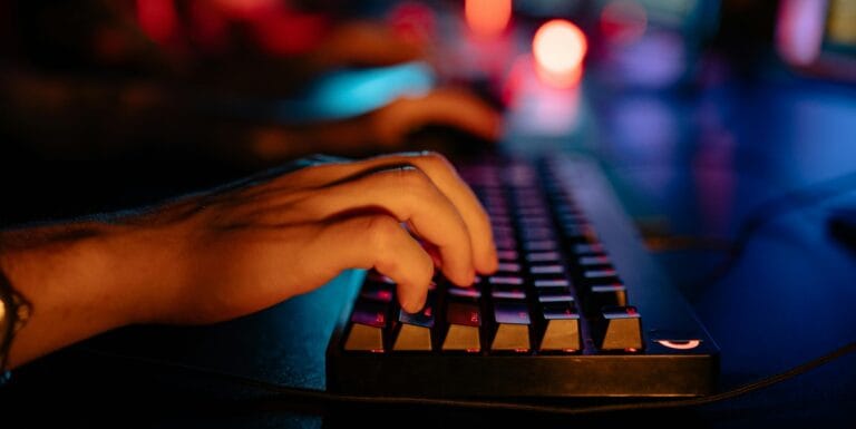 Fingers typing on an illuminated keyboard in a dimly lit room, creating a tech-focused atmosphere.